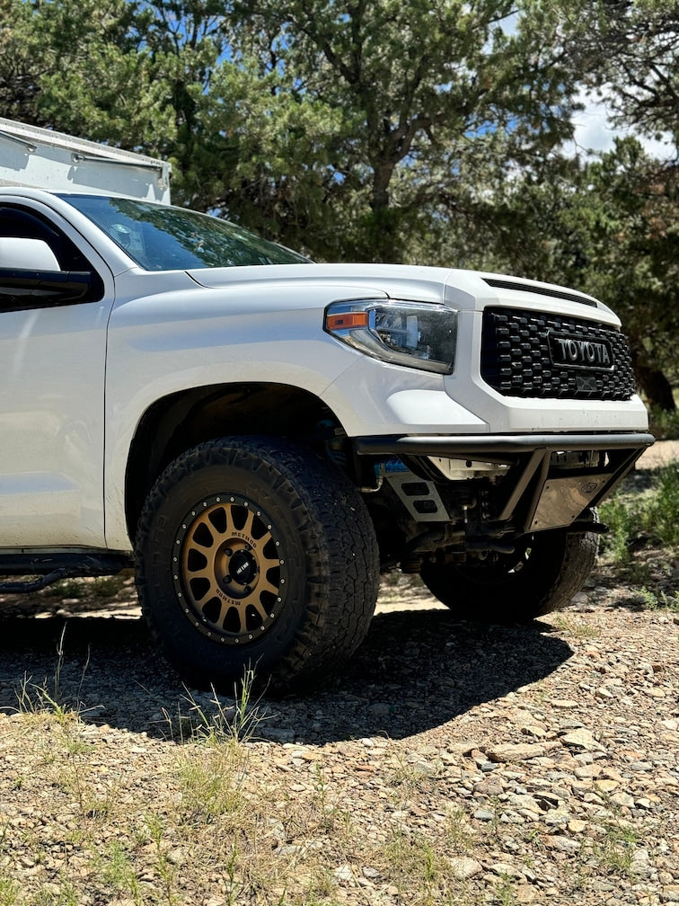 White Toyota Tundra off-road truck with a camper shell and bronze wheels on a dirt road. Explore with an RV rental.