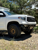 White Toyota Tundra off-road truck with a camper shell and bronze wheels on a dirt road. Explore with an RV rental.
