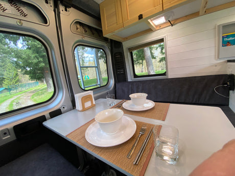 Cozy rv rental camper van interior. Dining area set for two with scenic outdoor views. Ready for adventure!