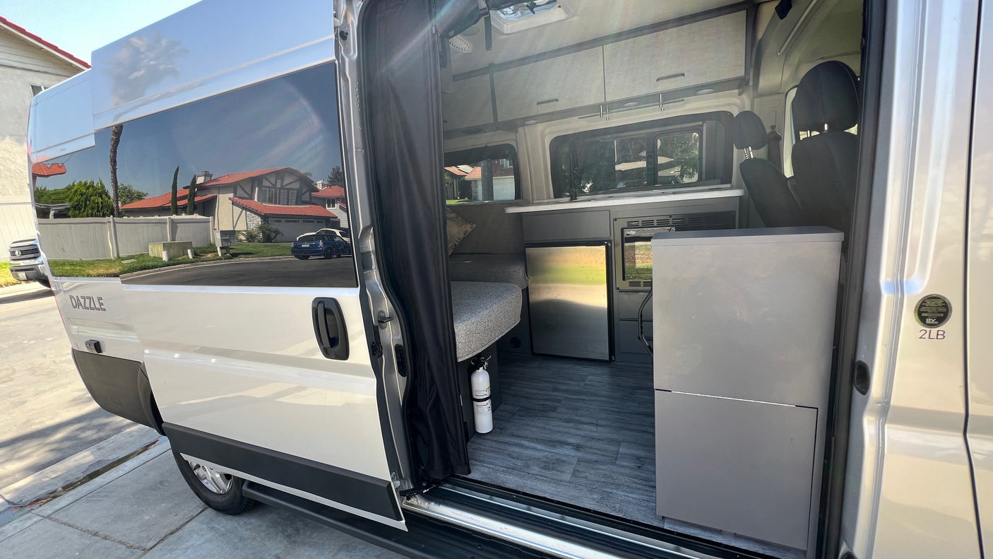 Interior of a modern van conversion RV rental, featuring a compact kitchen, fridge, and versatile living space.