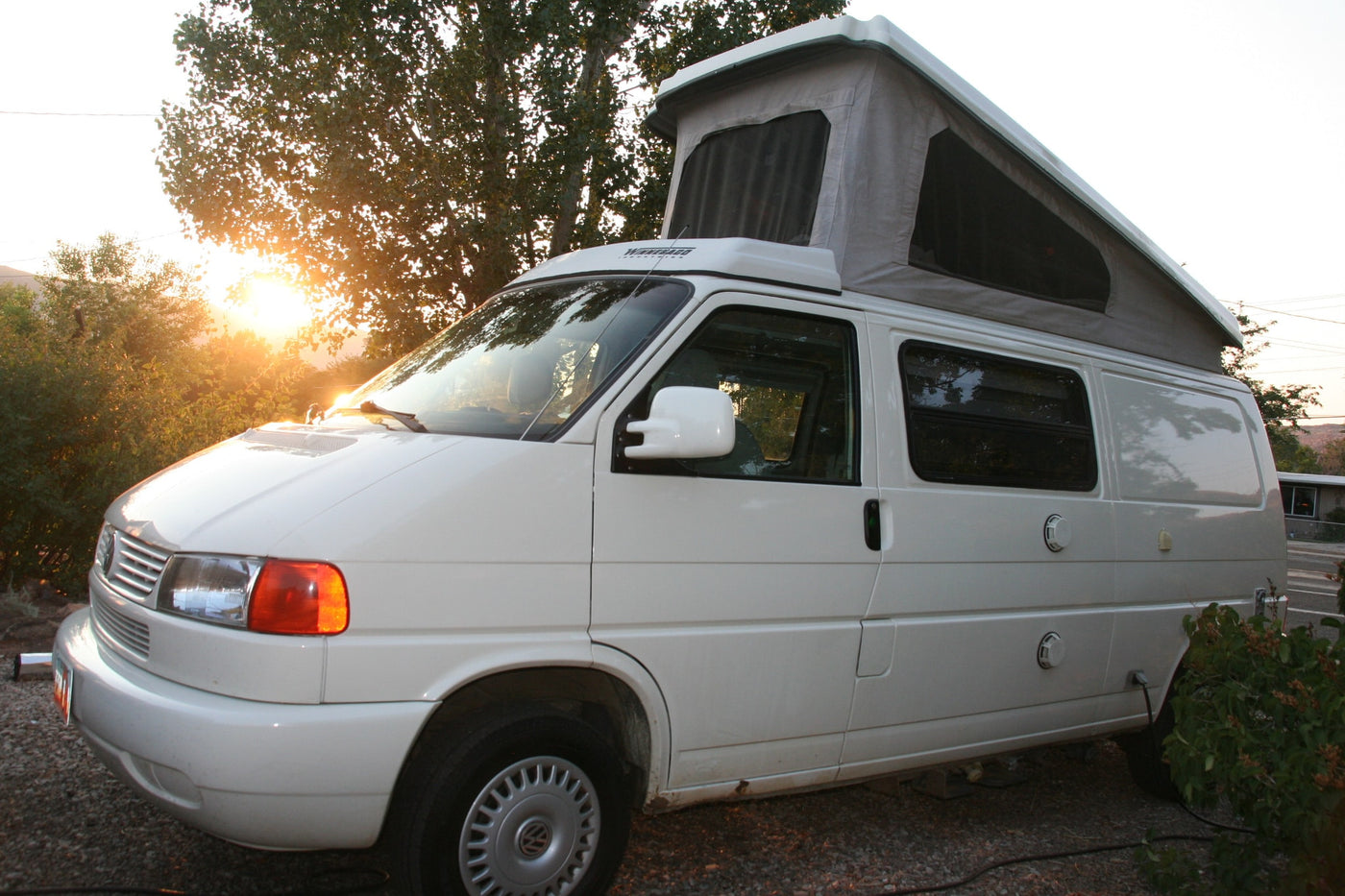 White Volkswagen Eurovan pop-top RV rental bathed in golden sunset light, ready for your next adventure. — photo 9