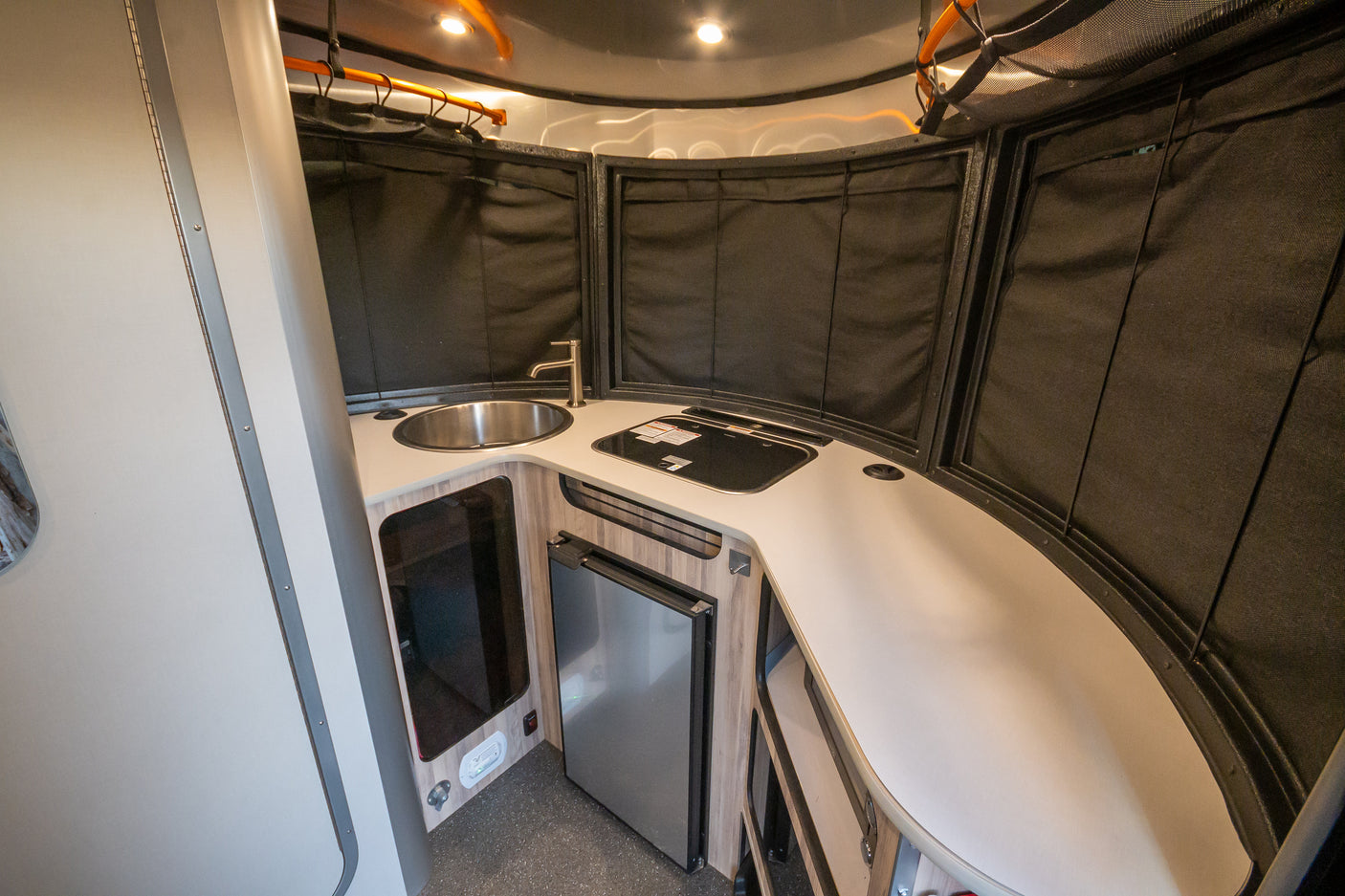 Modern and compact RV rental kitchen featuring a sink, stovetop, and refrigerator, ready for your travel adventures.