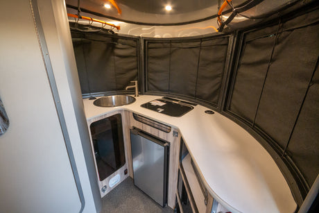 Modern and compact RV rental kitchen featuring a sink, stovetop, and refrigerator, ready for your travel adventures.