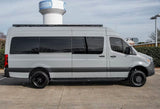 Side view of a light gray Mercedes-Benz Sprinter camper van, perfect for rv rental. Customized with a roof rack and black wheels.