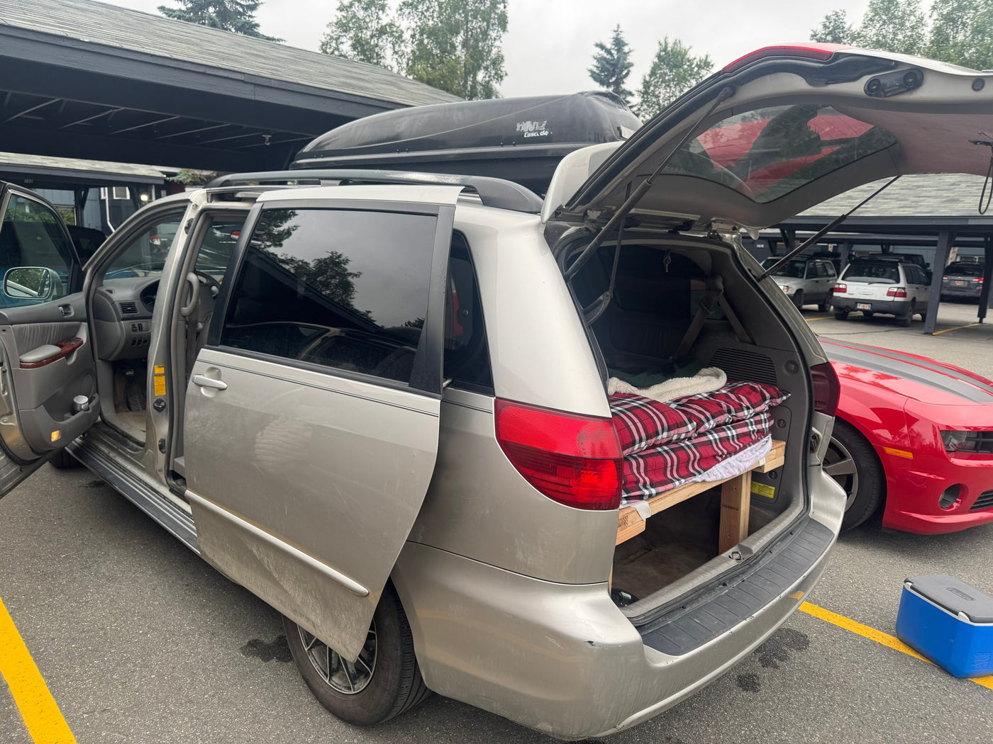  transforming it into a budget-friendly rv rental for road trips.|Dirty minivan with roof cargo box parked on gravel near an RV rental — photo 12