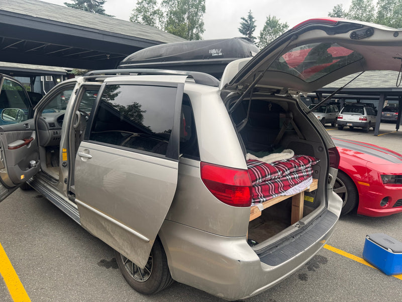  transforming it into a budget-friendly rv rental for road trips.|Dirty minivan with roof cargo box parked on gravel near an RV rental — photo 12