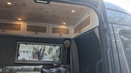 Cozy rv rental campervan interior: wood ceiling, rattan cabinets, window view, and soft seating for travelers.