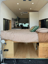 Inside a modern rv rental camper van: comfortable bed with gingham bedding, kitchen, and outdoor shower setup.