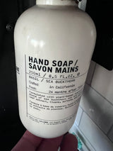 A close-up of a white Le Labo hand soap bottle, Basil/Sea Buckthorn scent, with product details visible. Ideal for any rv rental bathroom.