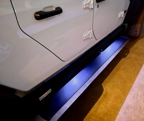Side of white vehicle with bright blue illuminated automatic running boards. Great for accessible entry, enhancing any rv rental journey.