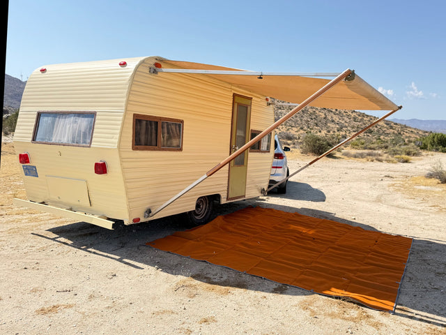 This vintage RV rental is set up for desert camping with its extended awning and ground mat