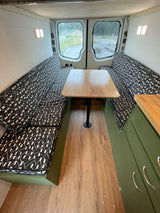 Inside an RV rental: a modern van conversion with geometric pattern bench seating, wood table, and green storage.