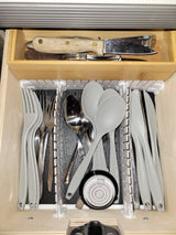 Compact RV rental kitchen drawer: Organized utensils (plastic/metal) including forks, spoons, knives, and a level tool.