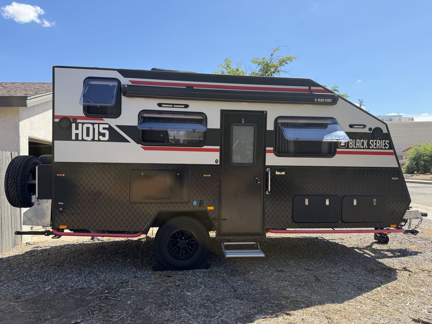 Passenger side of the HQ15 with the entry door closed and the pull-out step down, showing the awning rail along the roofline, three tinted windows, external storage hatches and the front-mounted spare tire — photo 2