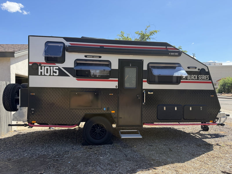 Passenger side of the HQ15 with the entry door closed and the pull-out step down, showing the awning rail along the roofline, three tinted windows, external storage hatches and the front-mounted spare tire — photo 2