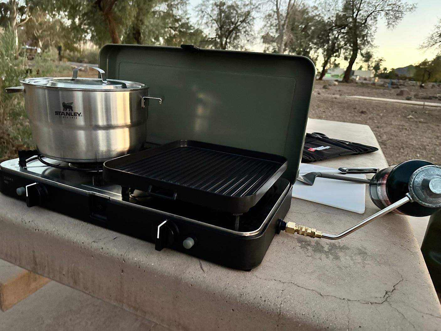 Preparing a meal on a dual-burner camping stove with a Stanley pot and grill, powered by propane, ideal for an RV rental trip.