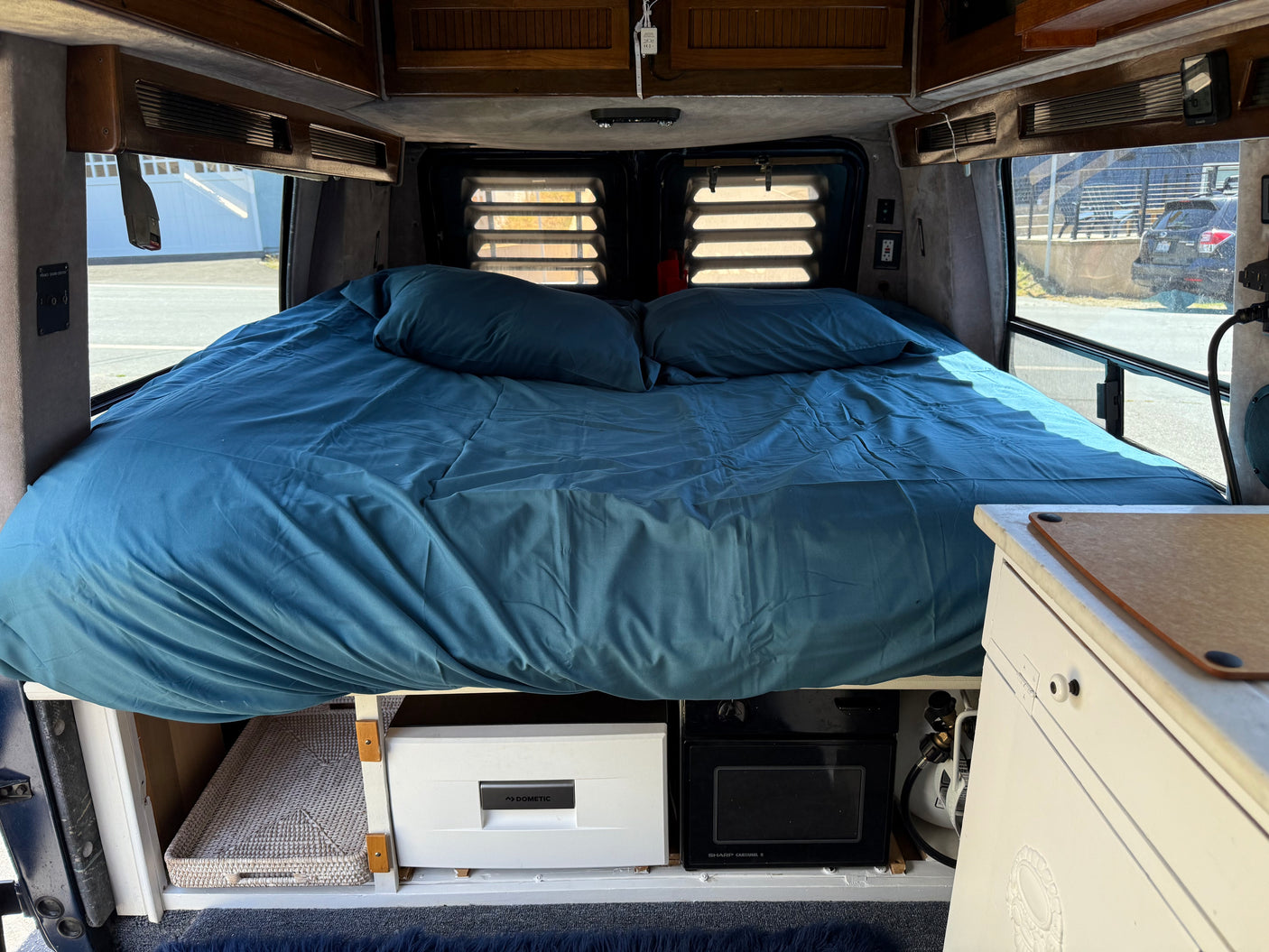 This RV rental offers a comfortable blue bed with under-bed storage, including a Dometic fridge and Sharp microwave.