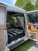 Open rv rental van interior showing front seats, cooler, striped rug, and wood accents. Ready for travel.