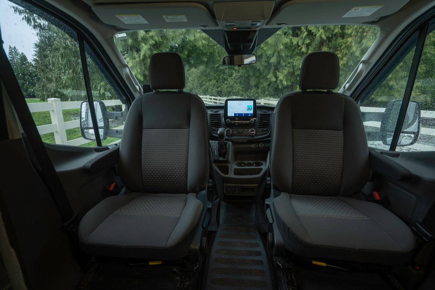 Inside an RV rental: front cabin with seats, dashboard display, and wet windshield view. — photo 13