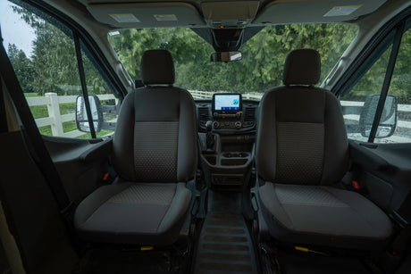 Inside an RV rental: front cabin with seats, dashboard display, and wet windshield view.