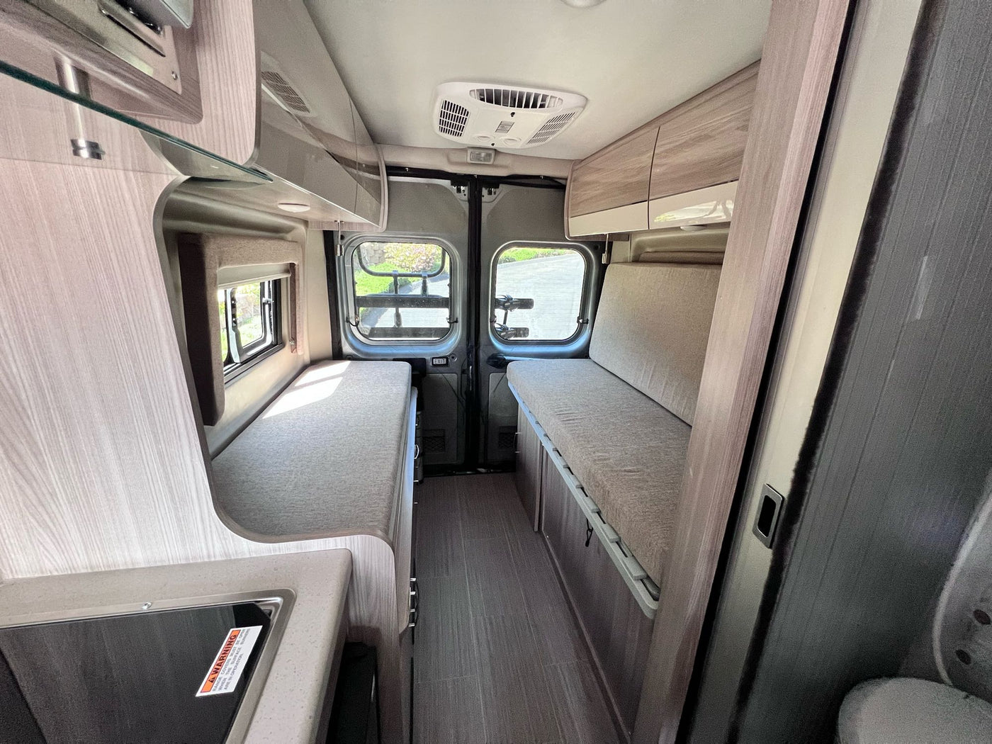 Inside an RV rental: a compact camper van interior with bench seating, kitchenette, and overhead cabinets. — photo 10