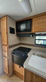 This clean RV rental kitchen features a microwave, stove, sink, and wood cabinetry, perfect for on-the-go cooking.