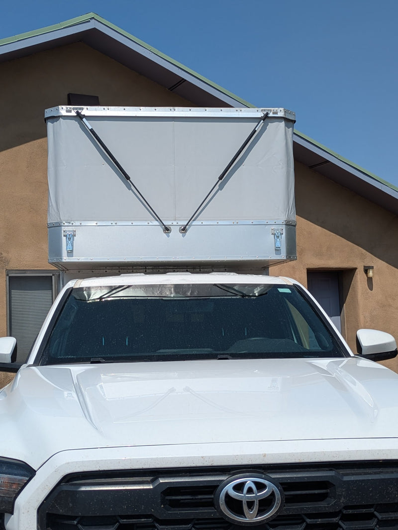 Pop-top camper roof raised, front three-quarter view of the Tacoma with juniper trees behind — photo 3