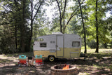Vintage rv rental parked at a serene campsite with a cozy campfire and chairs. Perfect for outdoor escapes.