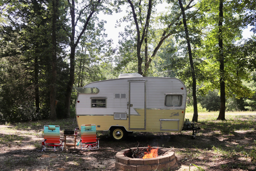 Vintage rv rental parked at a serene campsite with a cozy campfire and chairs. Perfect for outdoor escapes.