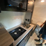 An RV rental's compact interior, showcasing a fully equipped kitchen with a stove, sink, microwave, and dinette.