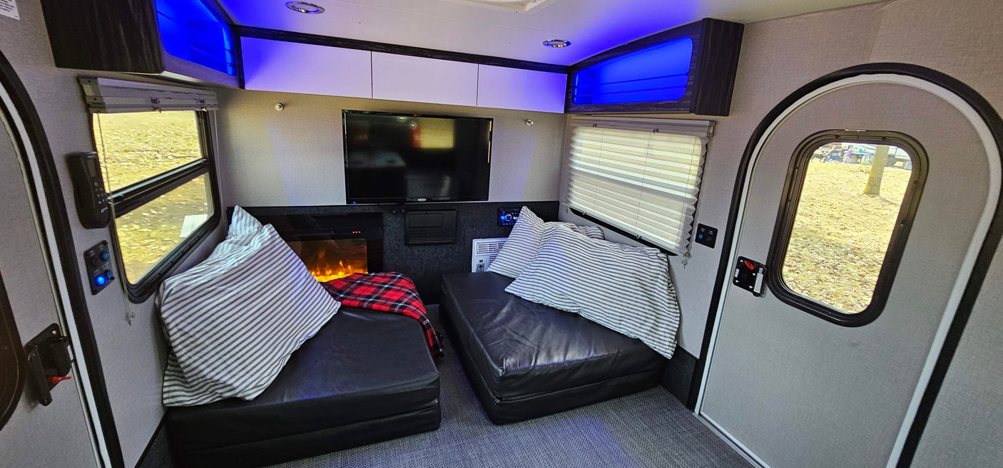Cozy RV rental interior with black lounge seating, TV, fireplace, and blue ambient lighting, perfect for travel comfort.