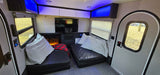 Cozy RV rental interior with black lounge seating, TV, fireplace, and blue ambient lighting, perfect for travel comfort.