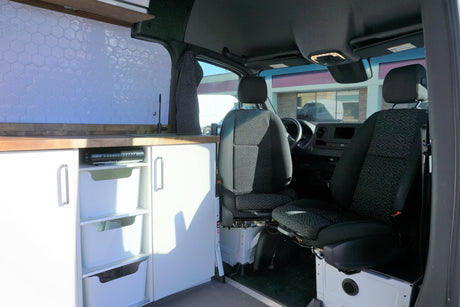 Custom rv rental: Modern campervan interior with tiled kitchen, wooden counter, storage, and front seats.