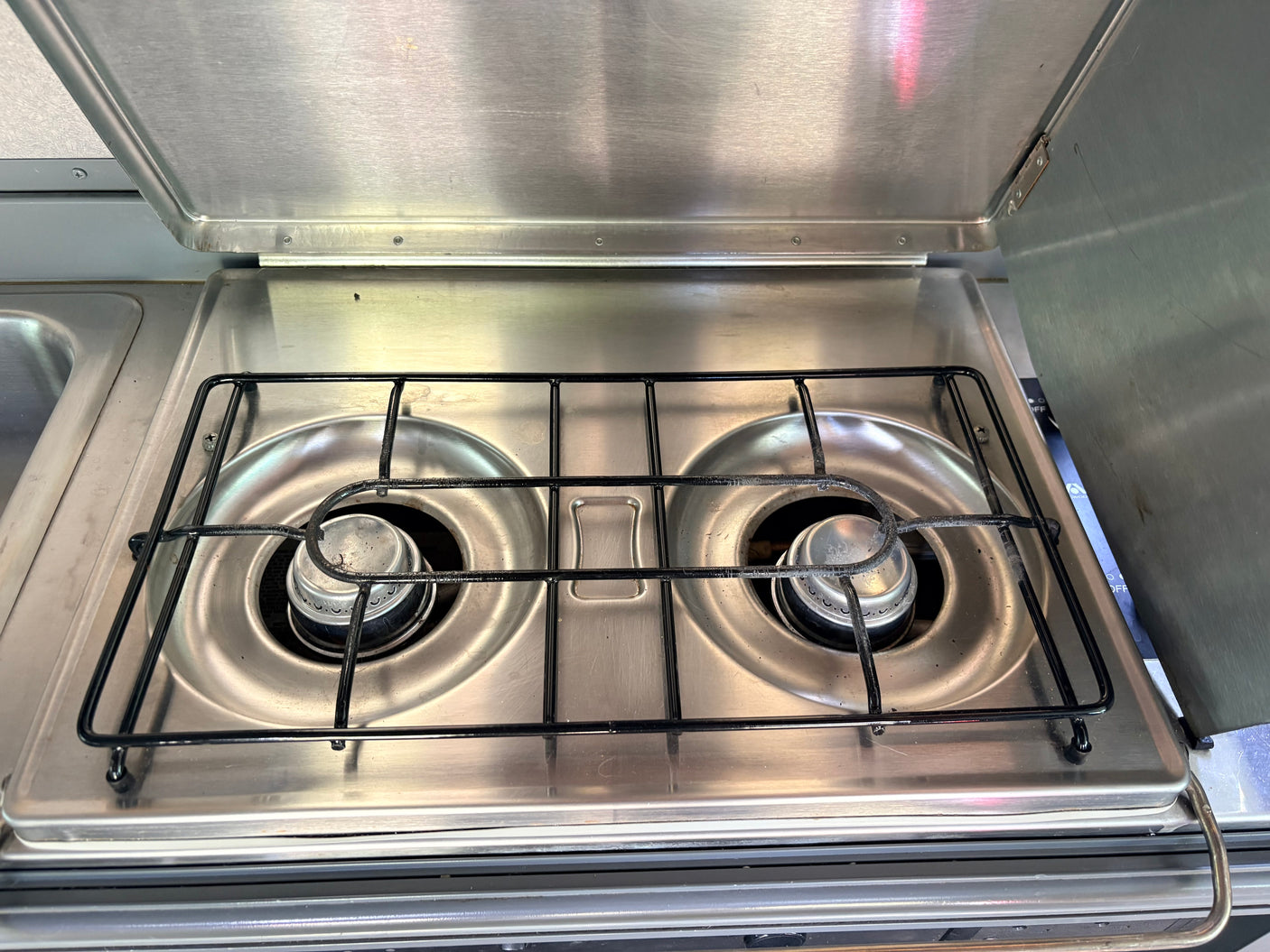 Stainless steel two-burner gas stove with lid open, ideal for cooking in an rv rental camper kitchen.