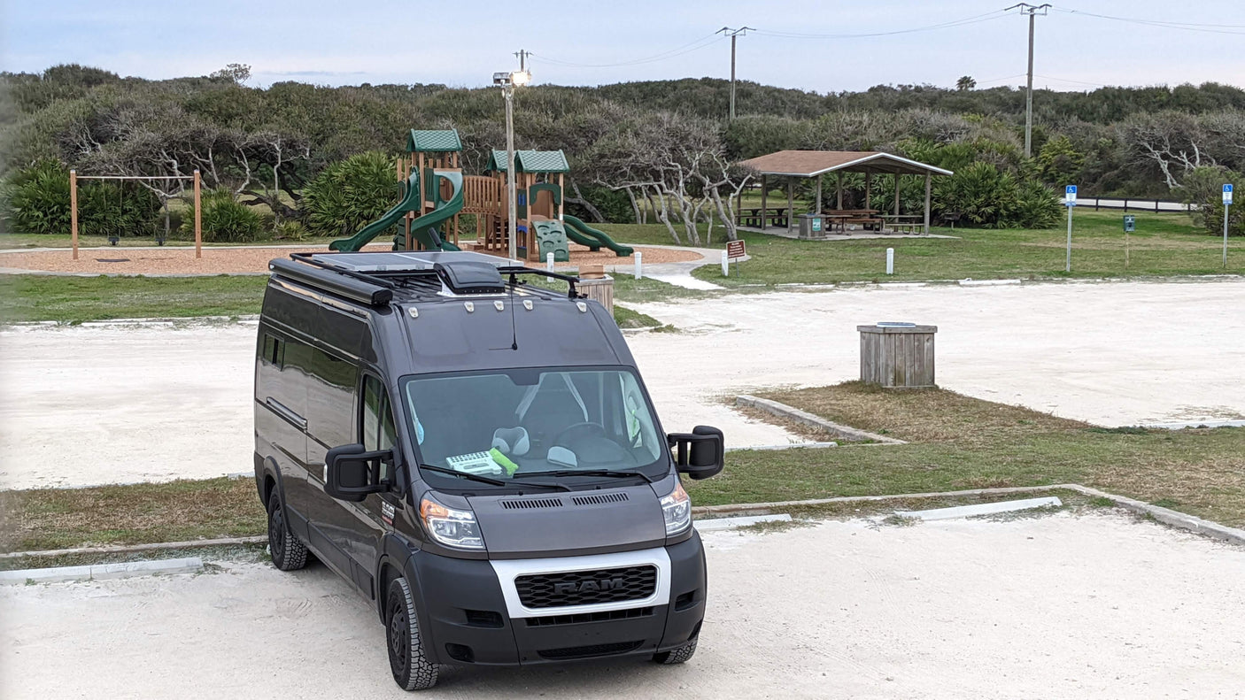 Gray Ram ProMaster RV rental parked at a serene outdoor park with a playground and picnic area.