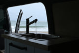 Enjoy ocean views from your RV rental kitchen! Water runs in the sink, with a beach and waves visible outside.