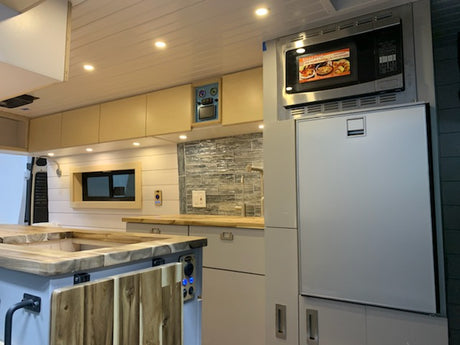 Inside a premium rv rental: a full kitchen with microwave, large fridge, custom counters, and storage.