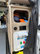 RV rental's compact interior: water utility panel with hookups, power outlet, and storage cubby.