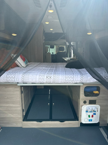 Cozy rv rental interior featuring a bed with a black pet, under-bed storage, and a water utility panel.