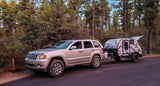 Explore nature with this RV rental: A beige SUV towing a modern Freesolo travel trailer in a quiet forest campsite.