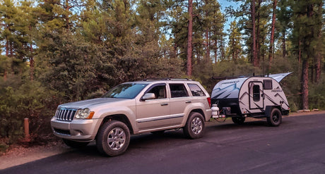 Explore nature with this RV rental: A beige SUV towing a modern Freesolo travel trailer in a quiet forest campsite.