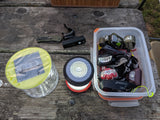 RV rental outdoor lighting essentials: solar lantern, headlamps in a bin, bike light, and knife on a wooden table.