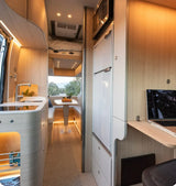 Explore this cozy RV rental interior: kitchen, dining, bed, and laptop workspace for scenic adventures.
