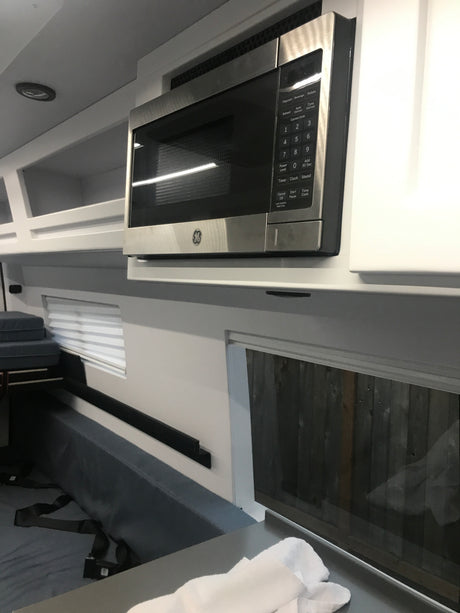 GE microwave in an RV rental interior, featuring white cabinets, a window, and comfortable seating.