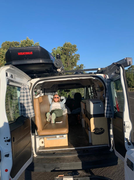 Relaxing in a custom rv rental camper van. A woman lounges on a bench, revealing a cozy interior with a cooler & storage.