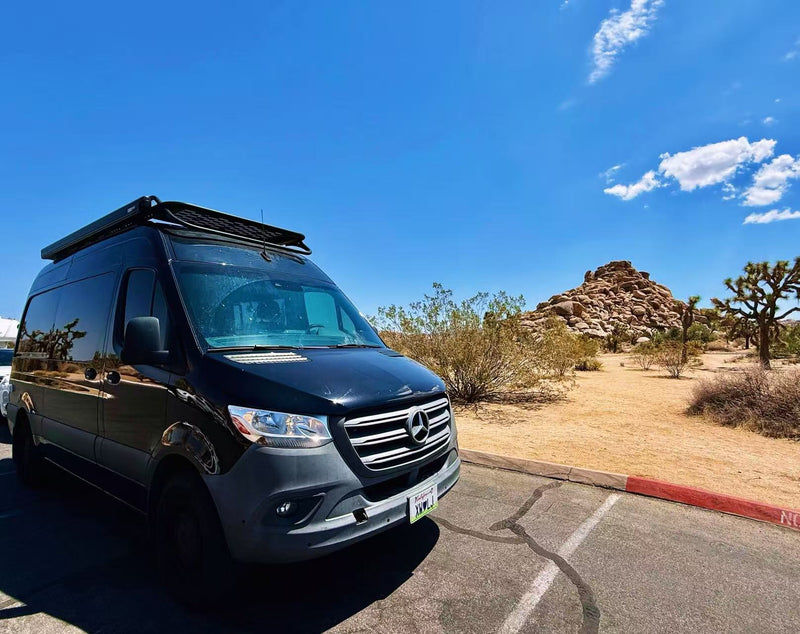 Black Mercedes Sprinter RV rental in a desert park with Joshua trees and rock formations under a blue sky.|Golden hour 'rv rental' setup: Black camper van with awning — photo 1