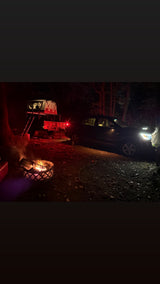 Night adventure camping with an RV rental alternative: a rooftop tent on a trailer, cozy campfire, and SUV under trees.