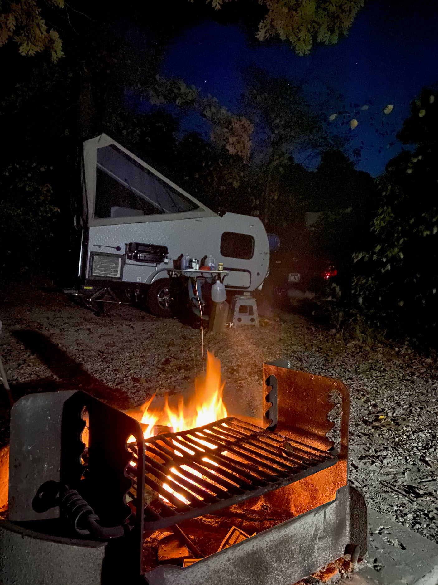 Cozy night camping with an RV rental: roaring campfire, pop-up camper, and starry sky.