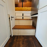 Cozy RV rental interior: Wooden steps lead to a yellow-quilted bed with storage, white cabinetry, and dark wood floors.