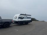 A dark gray pickup truck is hitched to a white and black Cherokee Wolf Pup travel trailer in a foggy parking lot, ready for an rv rental trip.
